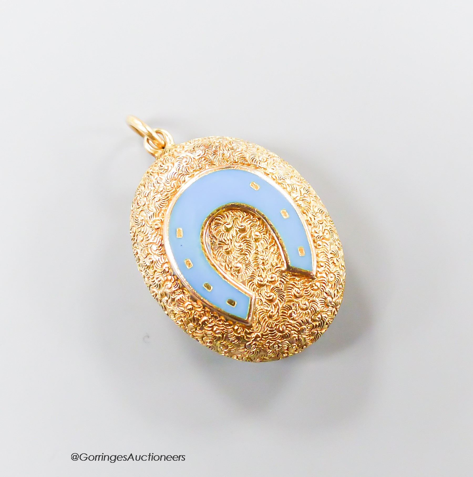 A Victorian style textured yellow metal and enamel set oval pendant, with horseshoe motif and glazed back, 23mm, gross weight 3.7 grams.